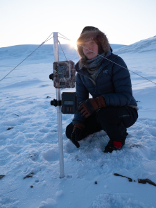 kvinne sitte rpå huk i snø med måleinstrument