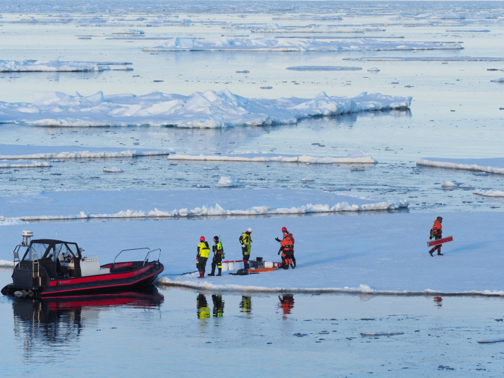 Forskere med utstyr og overlevelsesdrakter står ved en gummibåt på et isflak.