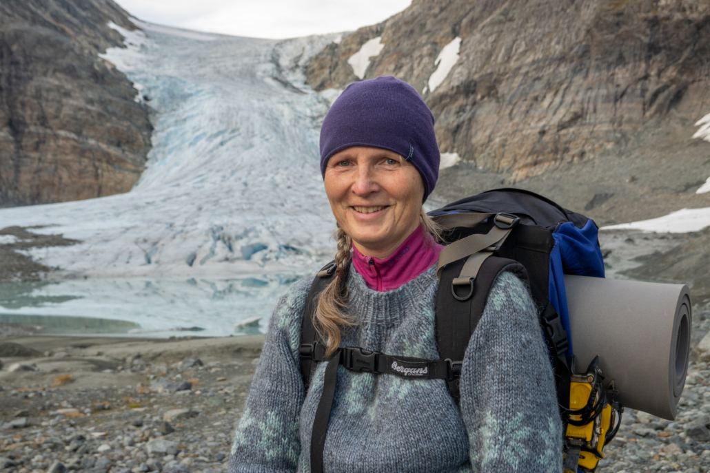 Kvinne med sekk på ryggen står foran en isbre
