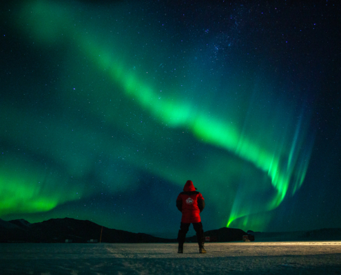 Mann står på isen og ser på fargene på himmelen