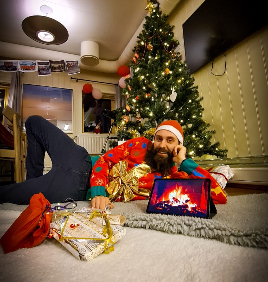 Mann ligger foran juletre med julegaver foran seg