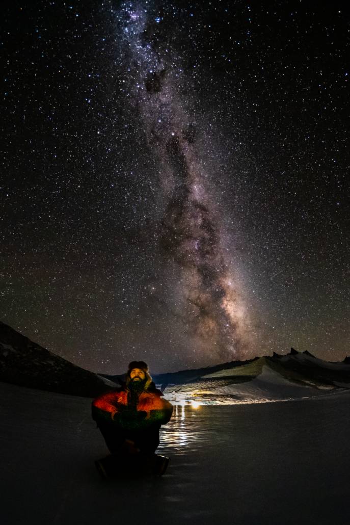 Mann sitter på isen og ser opp på stjernehimmel