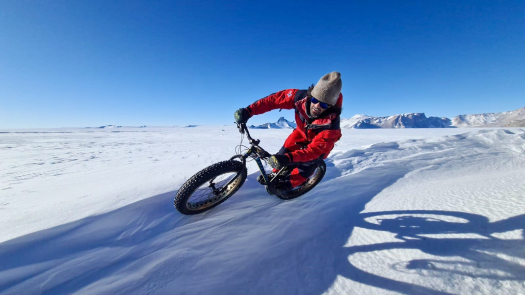 Mann sykler på snø med fjell bak