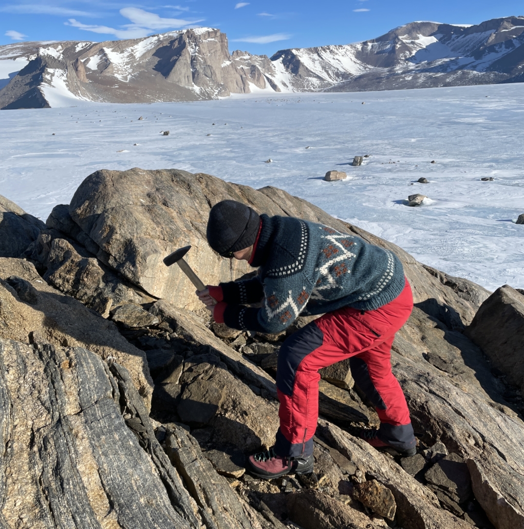 Kvinne med hammer står på steingrunn med is og fjell i bakgrunnen