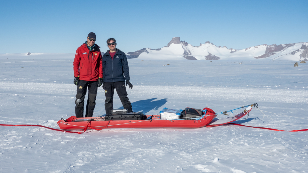 To personer står ved en slede med instrumenter. Fjell og is i bakgrunnen
