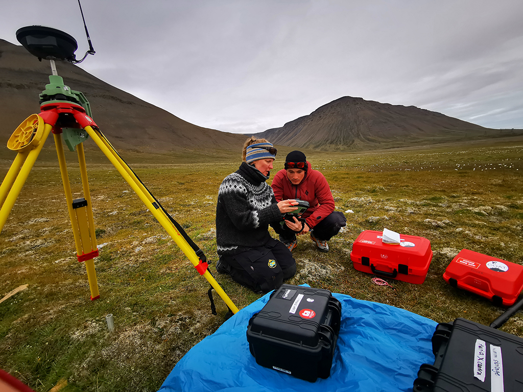 Kvinne og mann ser på et apparat, ved siden av ligger utstyr i kofferter og en apparat står på en tripod