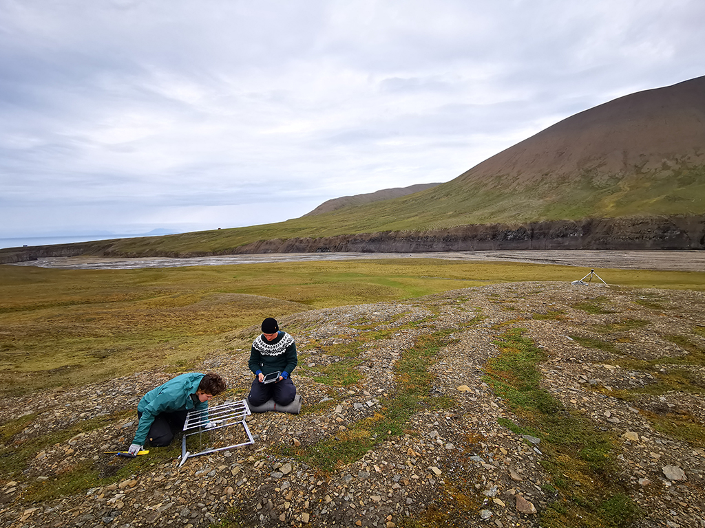 To forskere sitter på gresskledd bakke og jør målinger