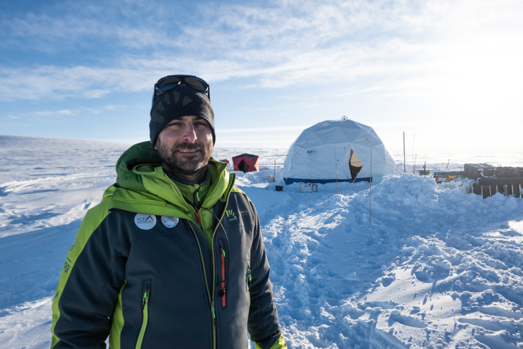 Person med jakke og lue står i snølandskap med telt i bakgrunnen